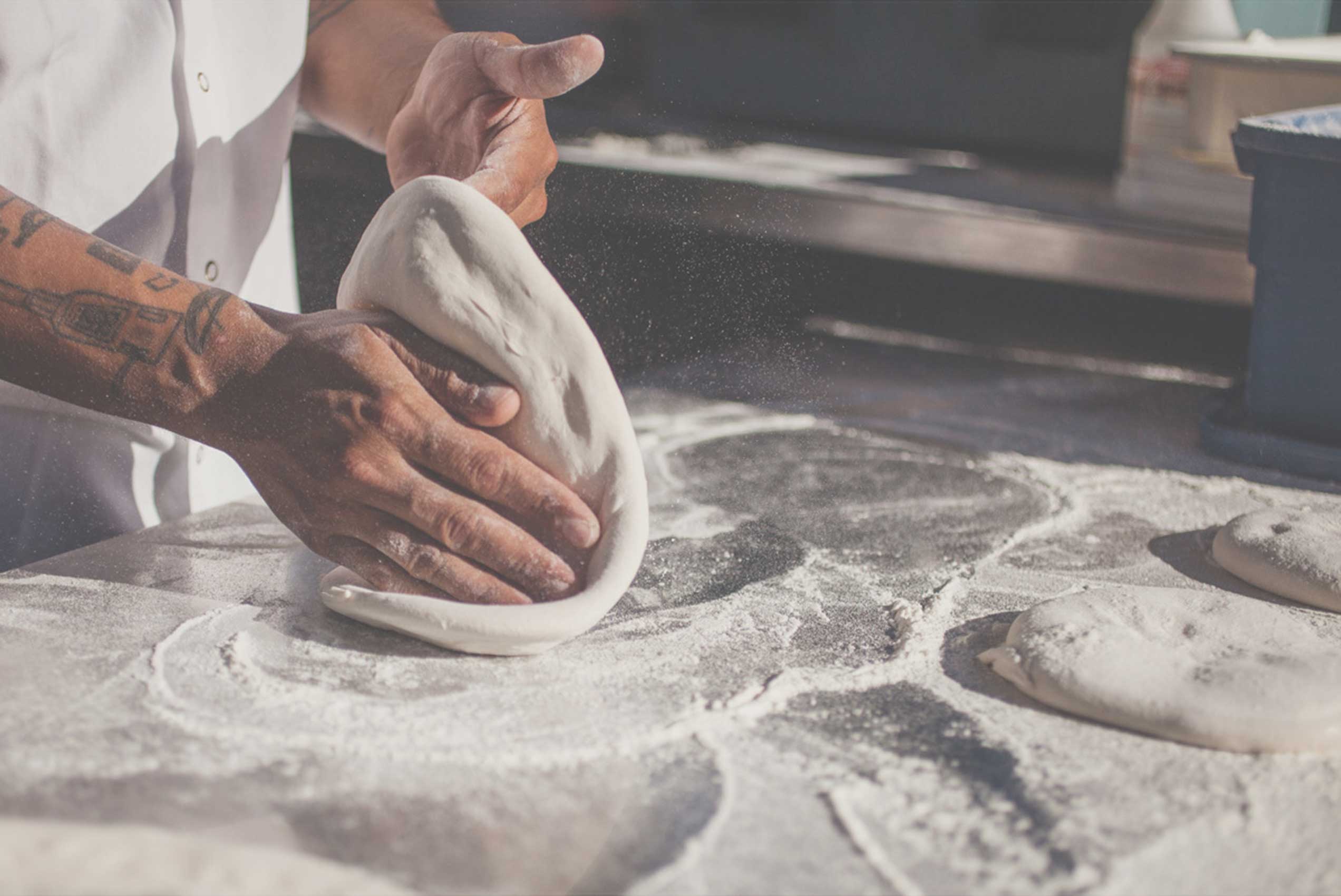 Two hands kneading pizza dough on floured surface in kitchen