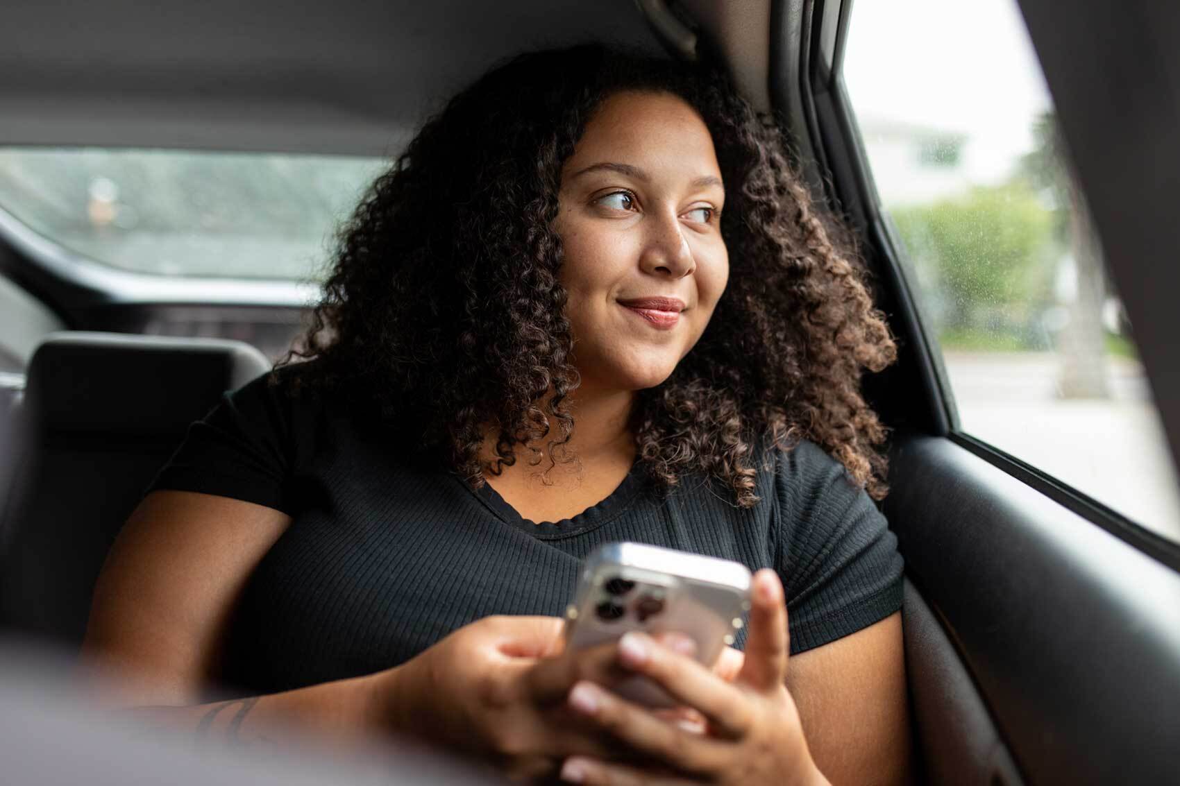 Smiling person sitting in parked car looking out the window while holding a phone